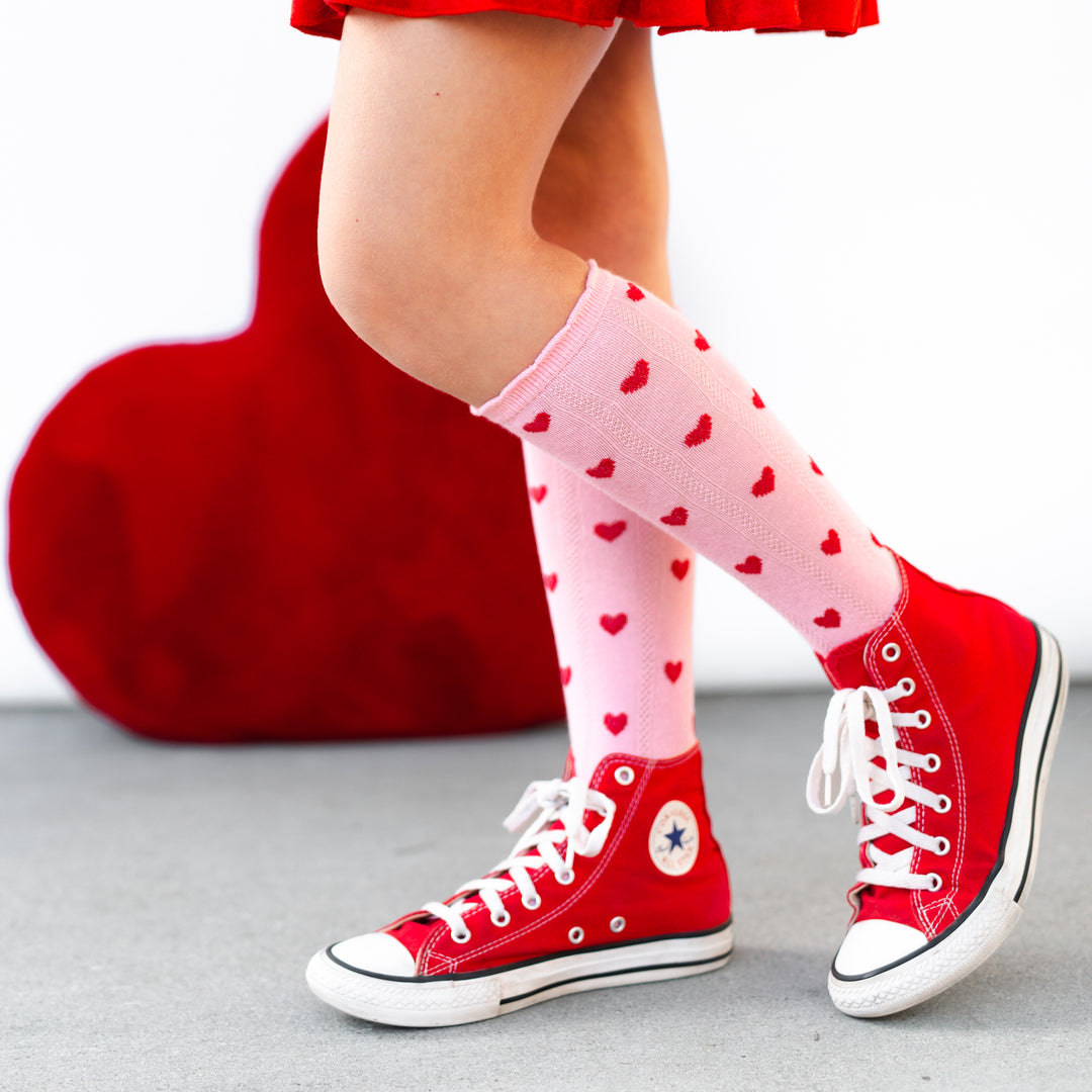 closeup of girls pink scalloped knee socks with red embroidered hearts pared with red velvet skort and red hi-top sneakers