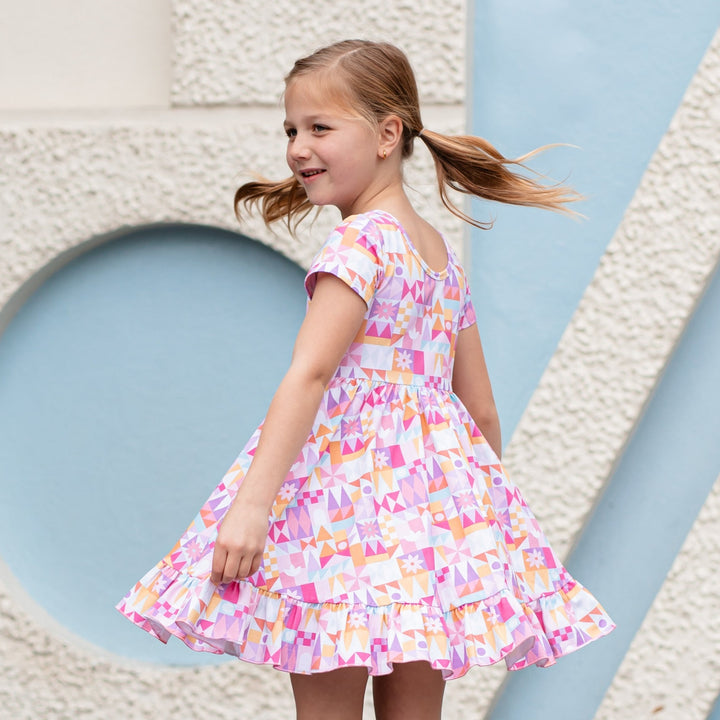 little girl with pigtails twirling in geometric print dress inspired by Disneyland's Small World