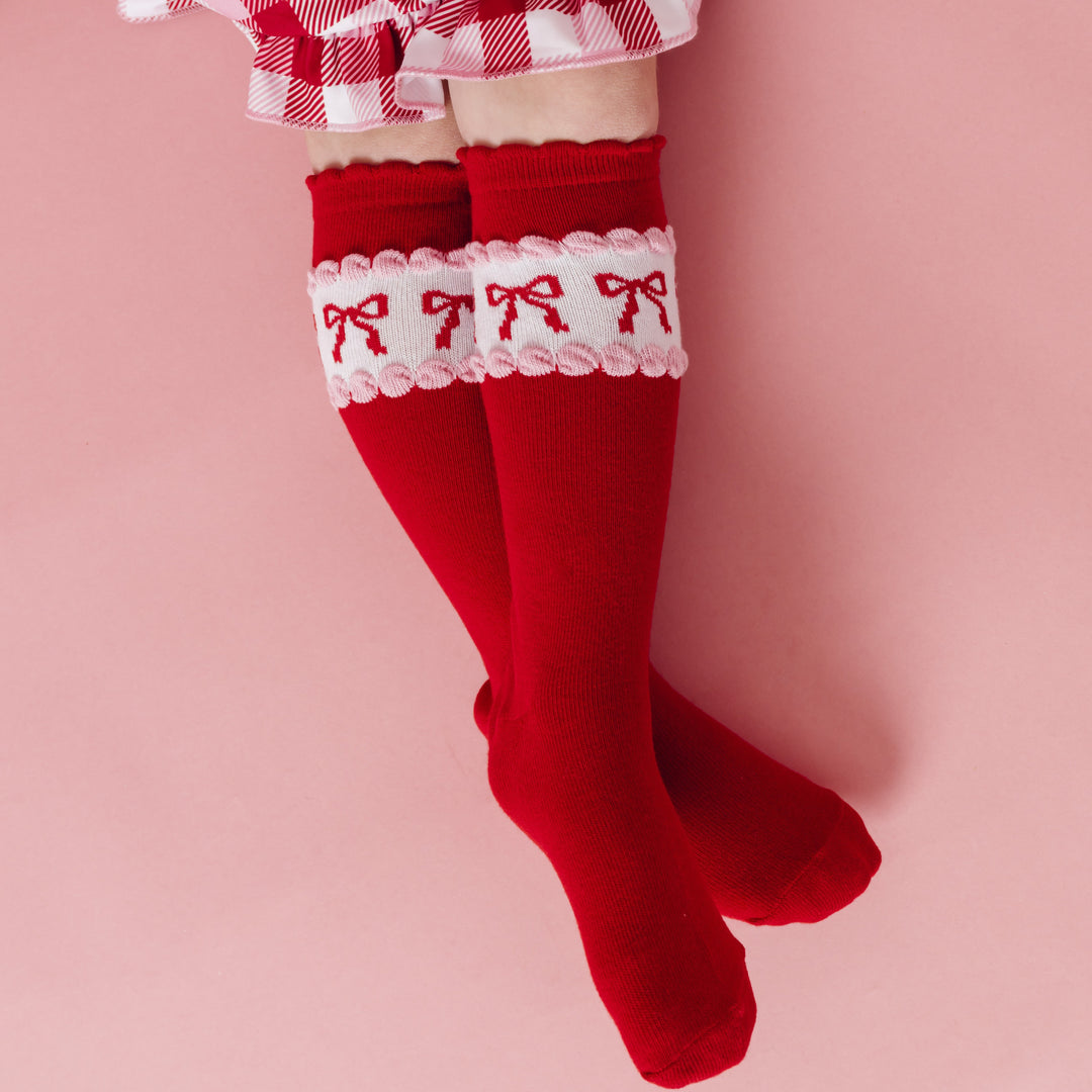 girl wearing bright red scallop trimmed knee socks with red bow design paired with red and pink plaid twirl dress