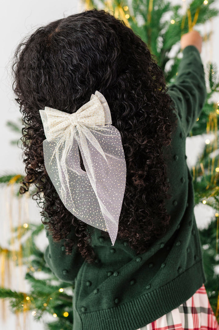 back of little girl decorating xmas tree with a vanilla cream sparkly hair bow in her hair.