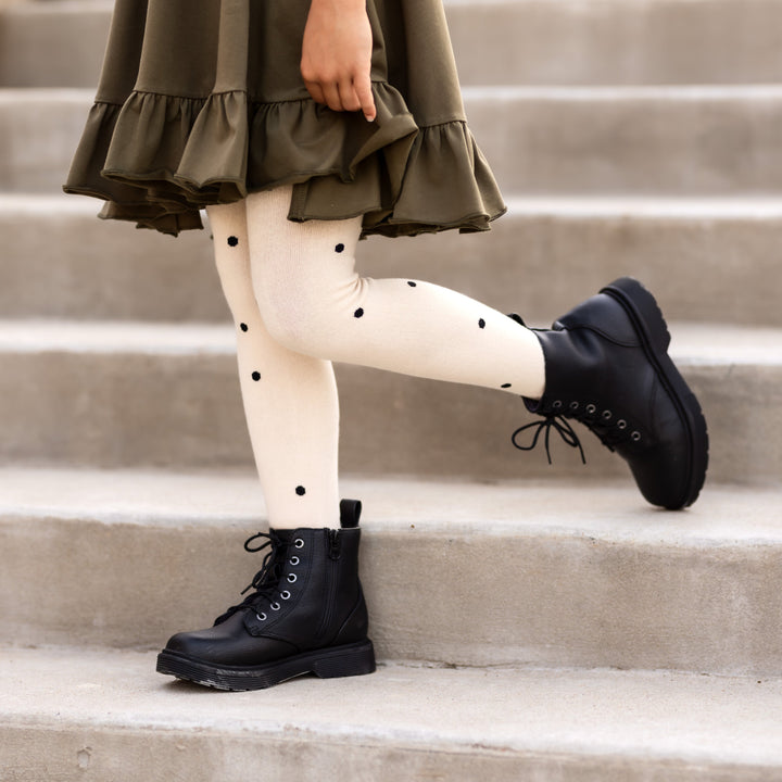 little girl standing on steps in vanilla polka dot pattern tights and black boots