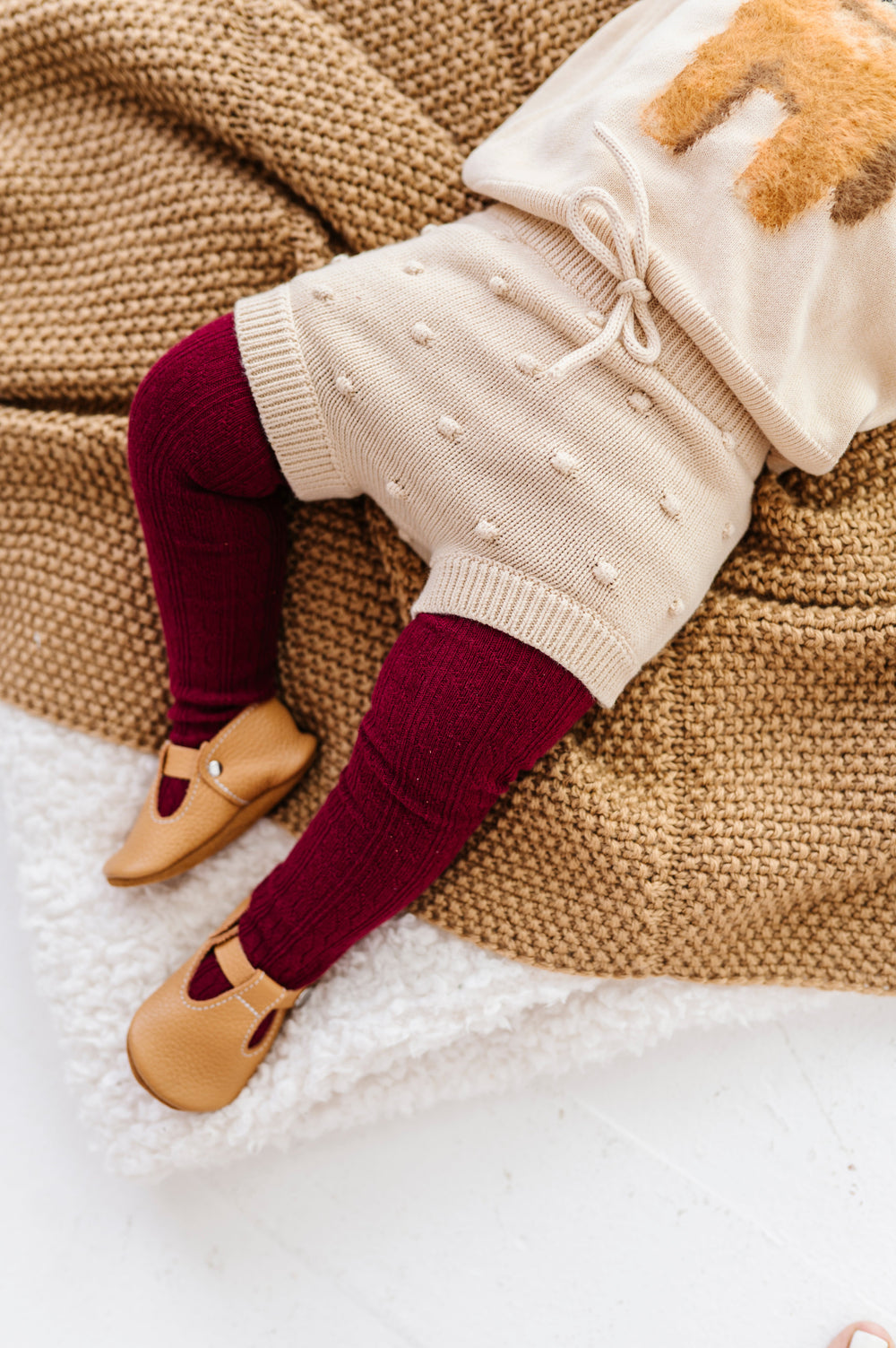 baby girl on blanket in cream knit bloomers with faux tie at the waist and 3D bubble texture paired with cream puppy sweater and burgundy cable knit tights