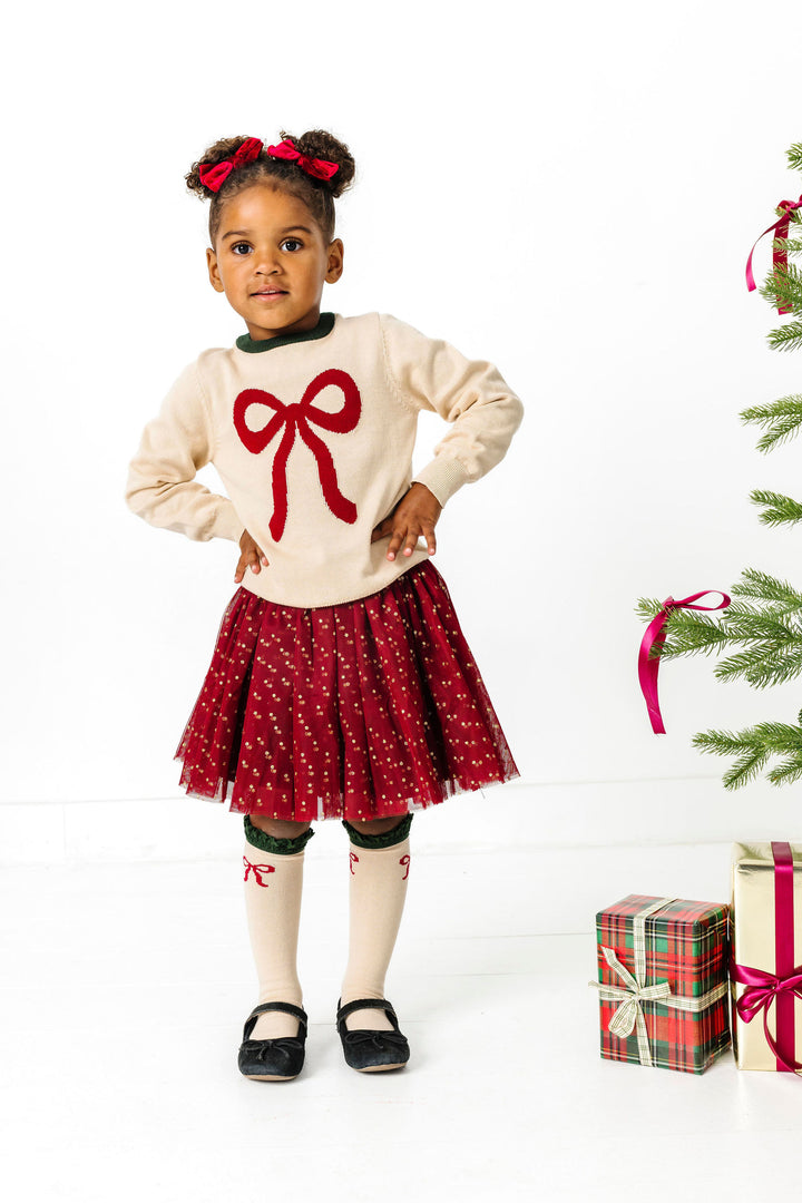 little girl in crimson and cream bow sweater, tutu skort, satin pigtail bows and matching bow knee socks for Christmas