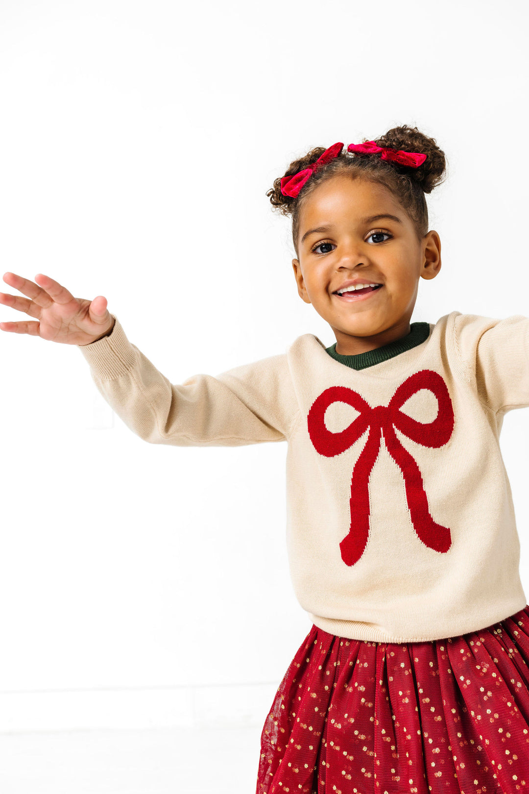 girl in cream holiday sweater with red bow design paired with crimson tutu skirt with sparkly gold dots