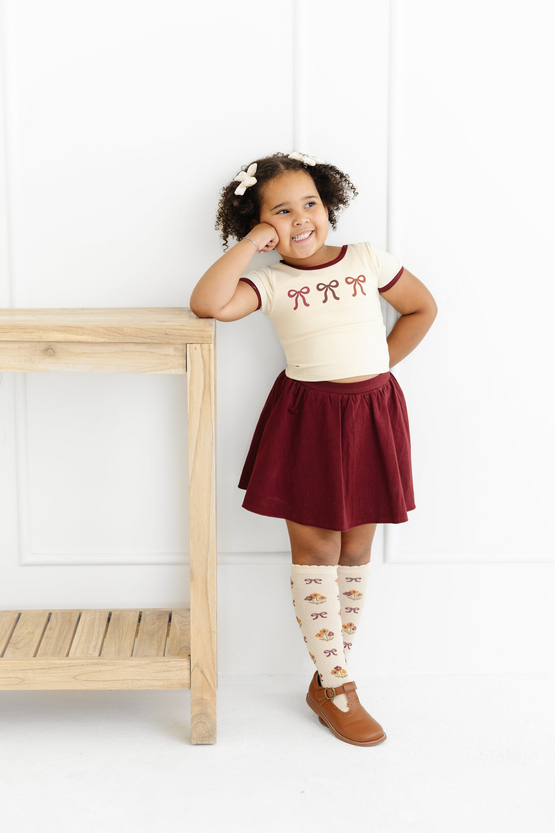 little girl in cream and burgundy outfit with bow print top, burgundy skort and matching socks and bow for fall
