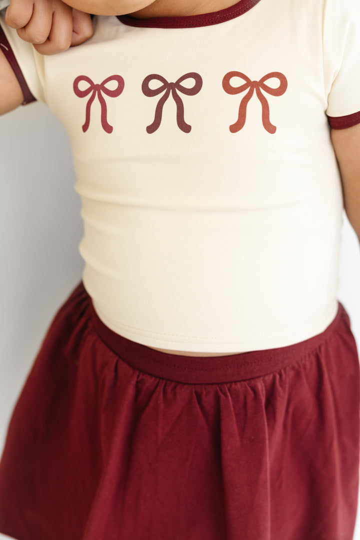 closeip of cream top with burgundy binding and bow print paired with matching burgundy skort