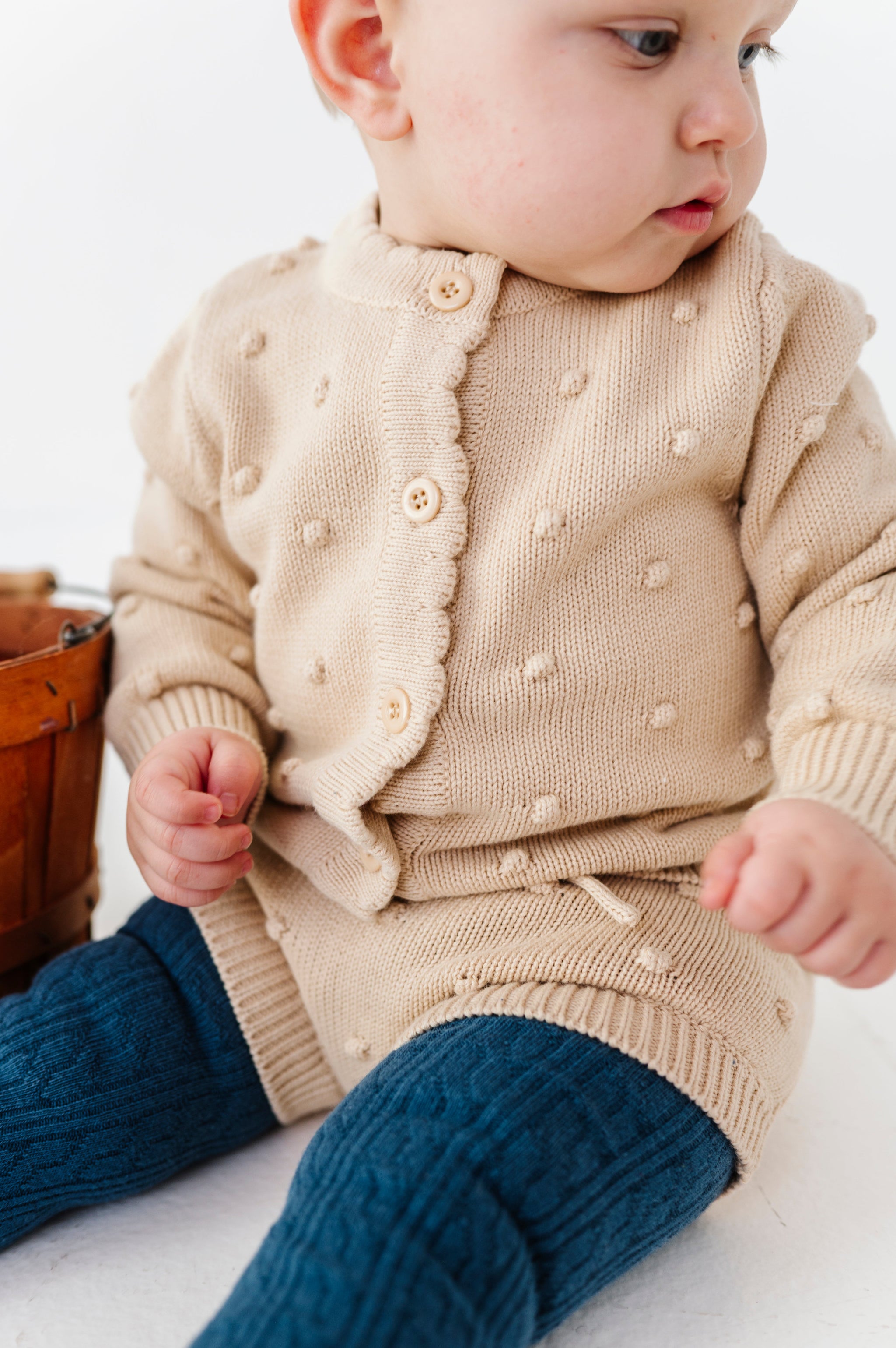 baby girl in button front vanilla cotton knit cardigan with 3D bubble design paired with matching knit bloomers and blue cable knit tights
