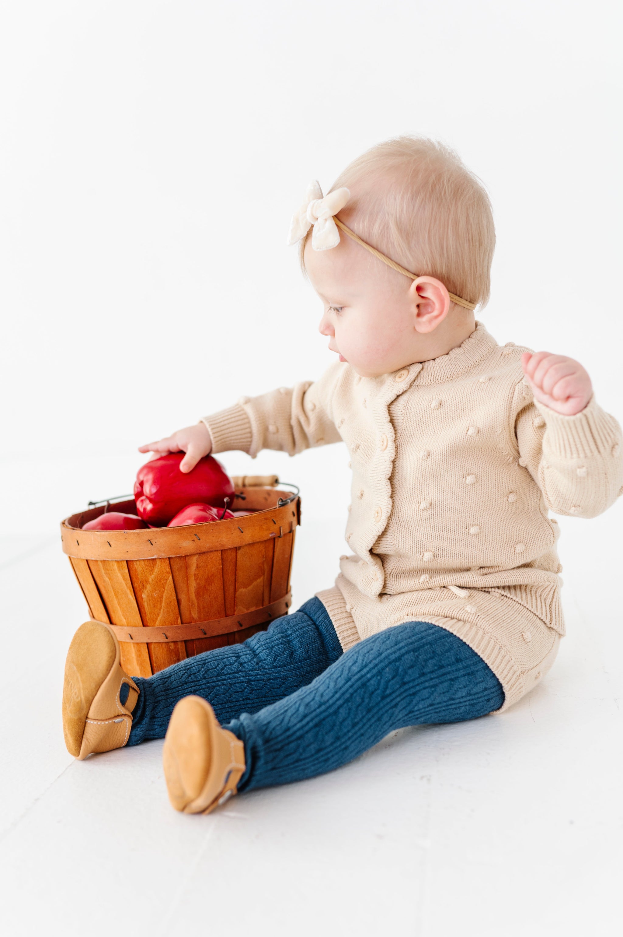 baby girl with apple basket in cream 3D bubble knit cardigan and bloomer set paired with matching cream velvet bow and fall blue cable knit tights