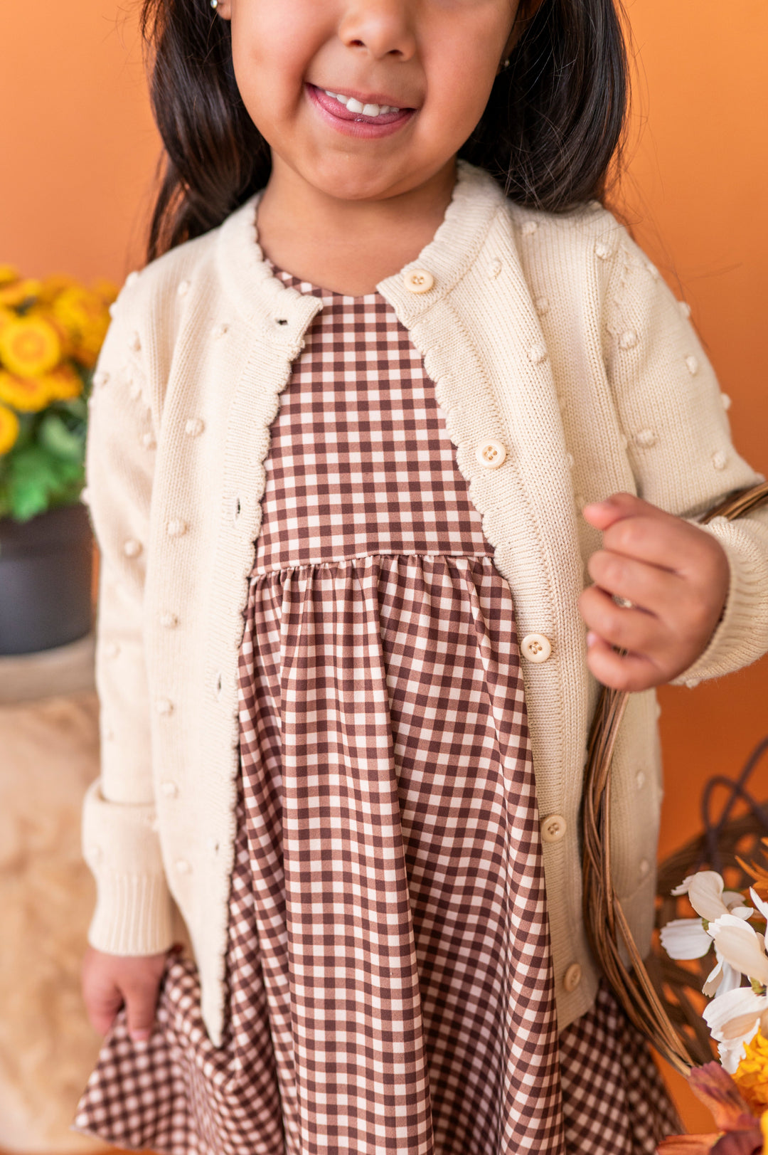 young girl in cream cotton knit cardigan with 3D bubble design paired with brown gingham twirl dress