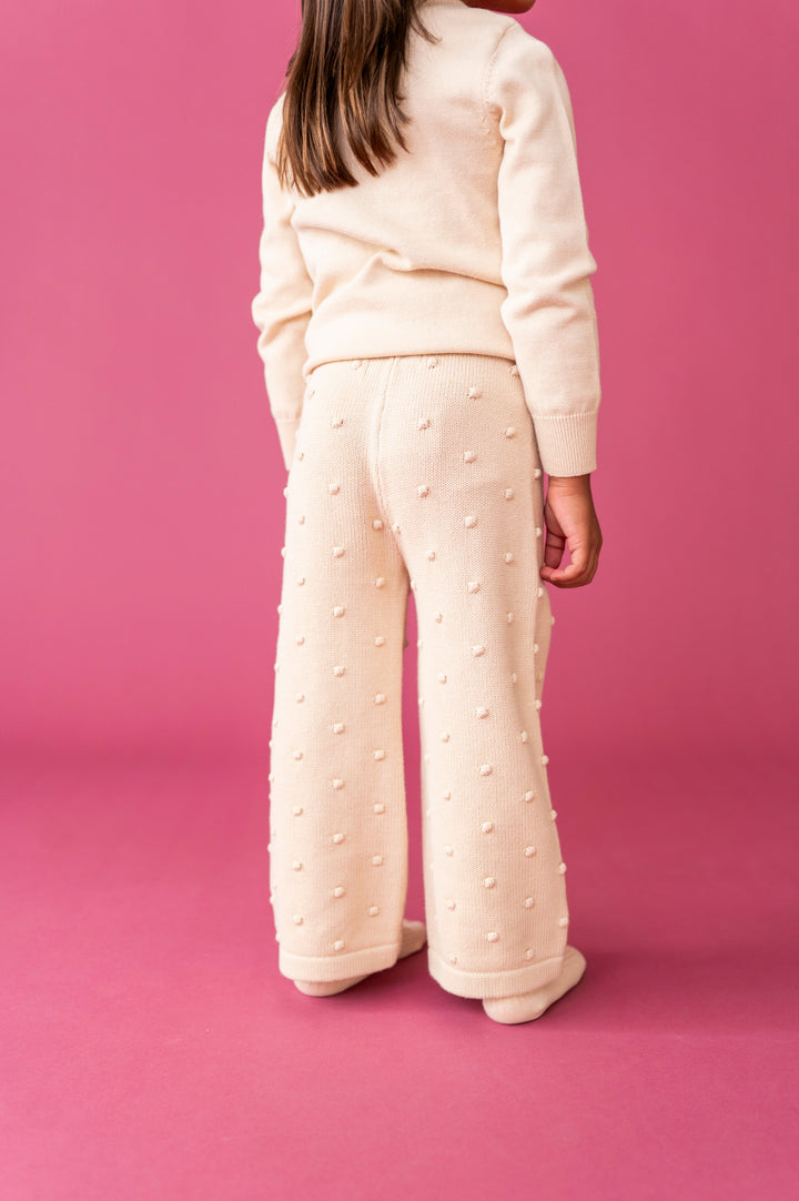 little girl with cream knit sweater pants featuring raised bubble texture and  with matching cream sweater