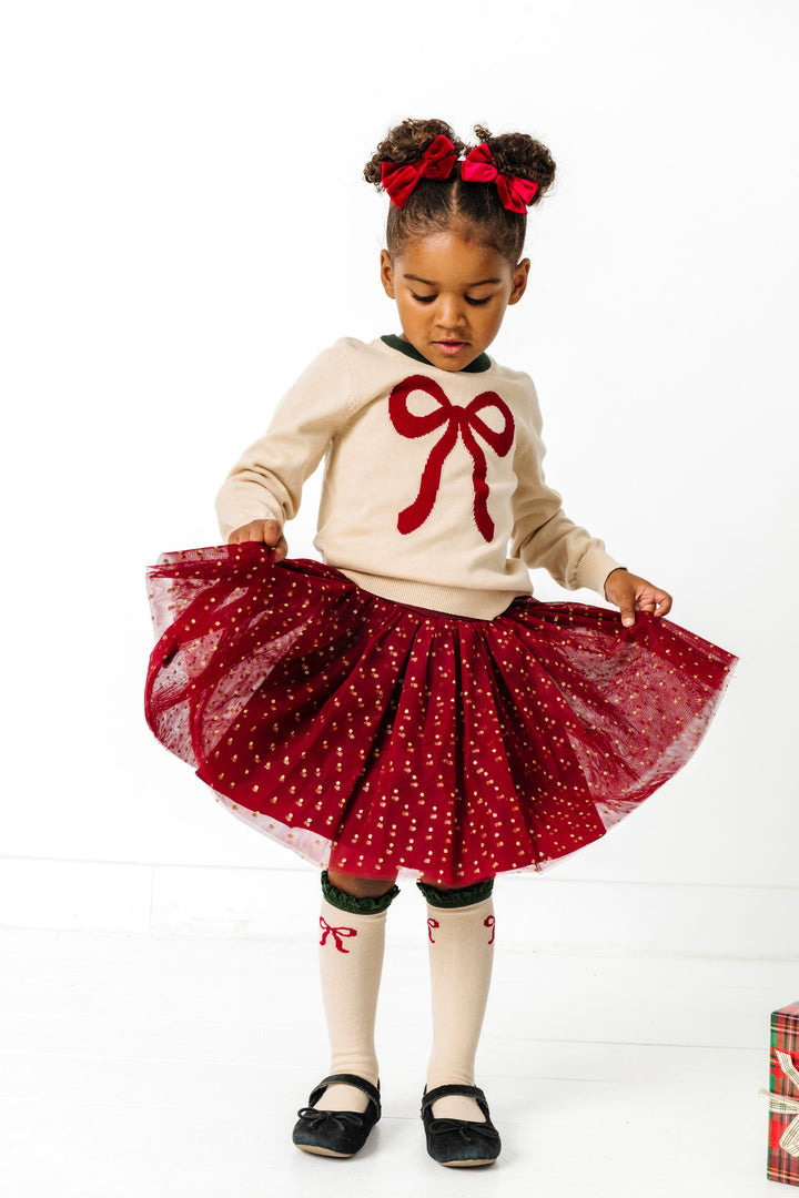 little girl in crimson and cream bow sweater, tutu skort, velvet pigtail bows and matching bow knee socks for Christmas