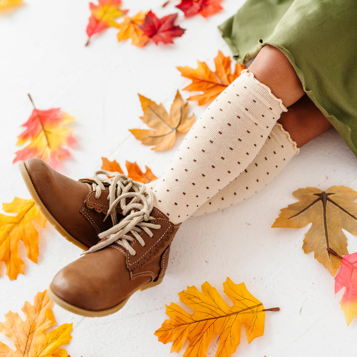 girl sitting in fall leaves wearing cream lettice trim knee socks with brown dot pattern and brown ankle boots