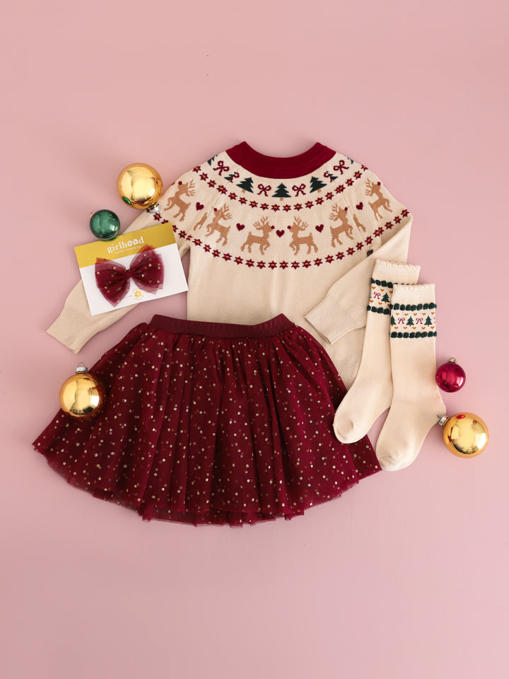 flat lay of girls' cream pullover sweater with fair isle reindeer design, crimson tutu skirt with gold sparkly dots, matching tutu bow and tree socks