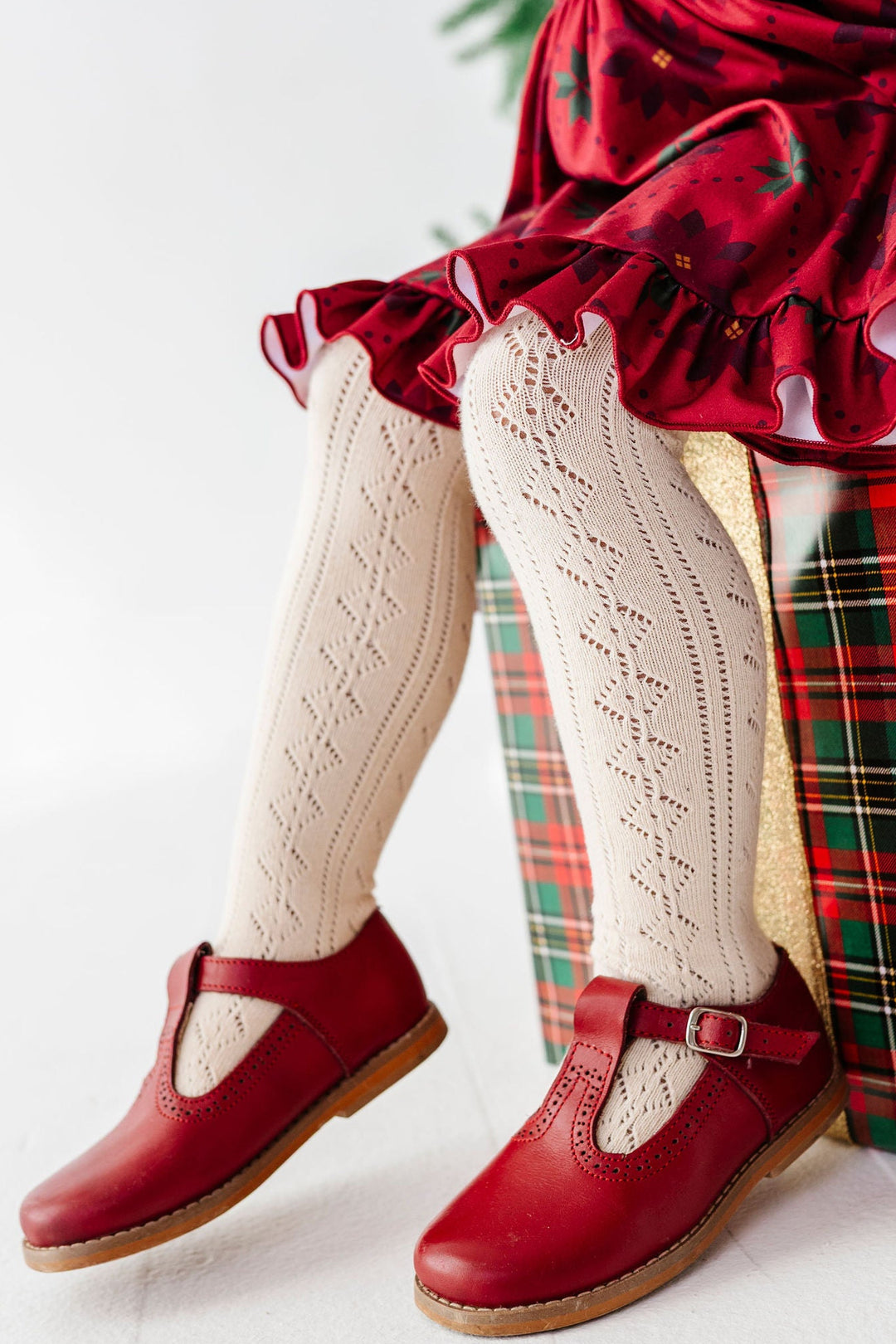 girl sitting on a christmas gift wearing cream colored pointelle knit tights and a poinsettia print christmas dress