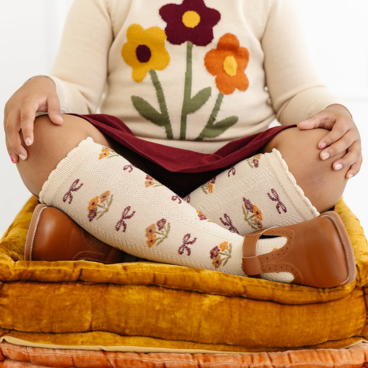 little girl in cream sweater with fall floral bouquet design with matching vanilla scallop trimmed knee highs with floral and bow design