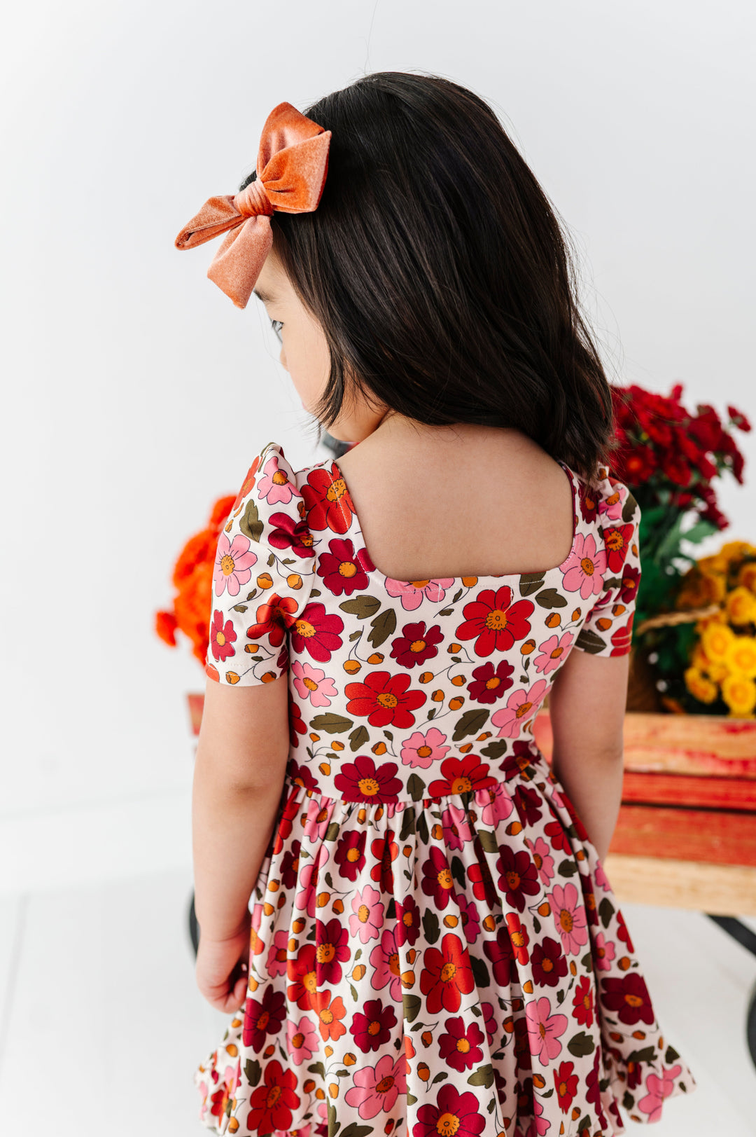 young girl in square neck cream with fall floral print twirl dress paired with rust velvet hair bow