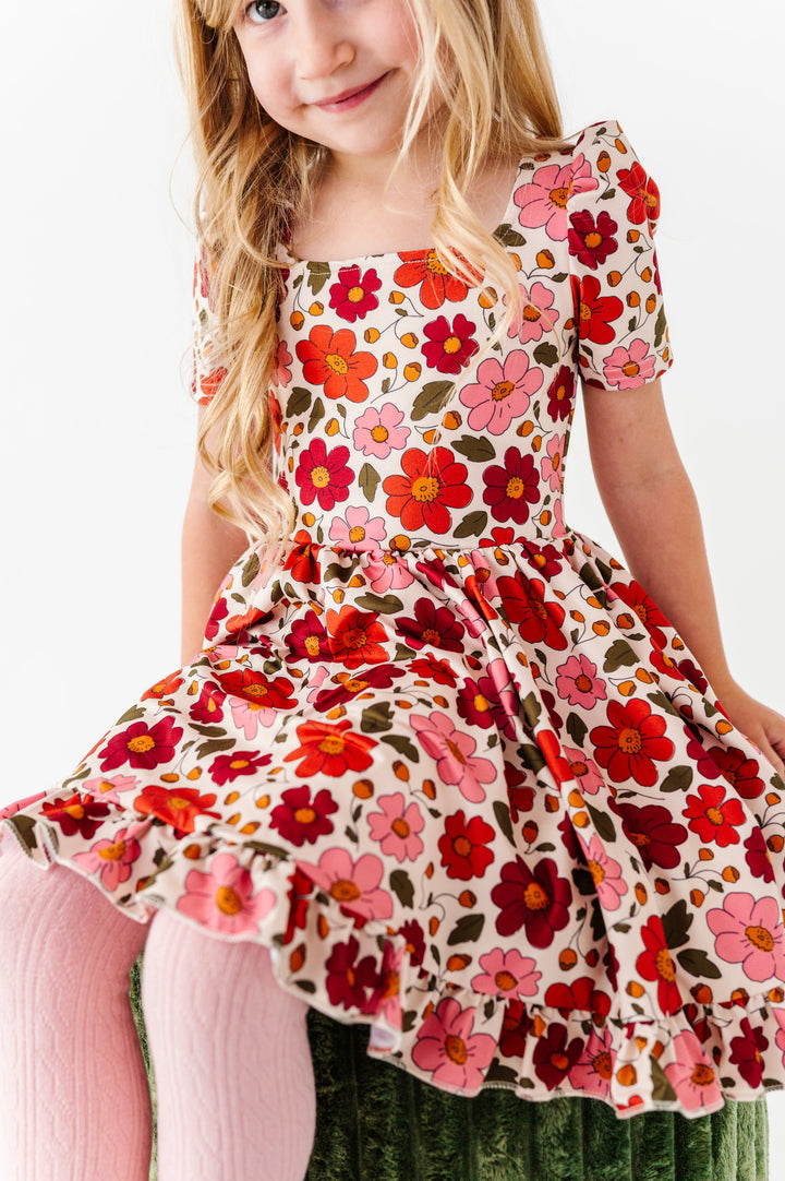 little girl sitting on green velvet stool in fall floral twirl dress on cream paired with coordinating light pink cable knit tights