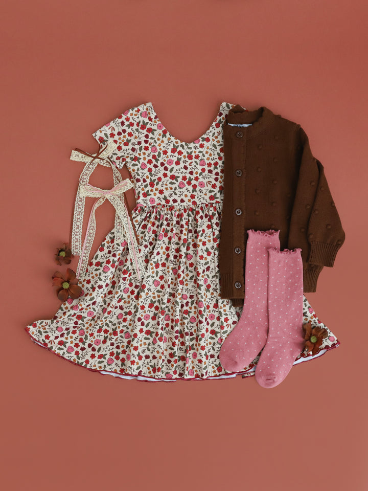 styled flat lay photo of girls cream floral twirl dress paired with matching brown knit cardigan, rose dottie knee socks and lace ribbon hair bows