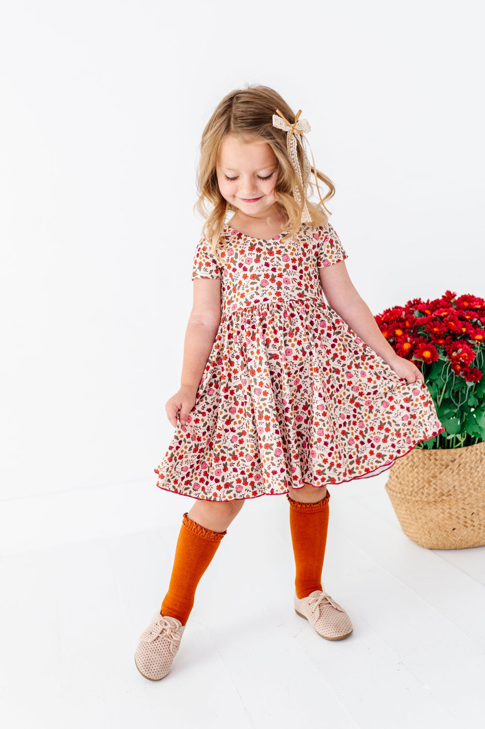 young girl in cream fall floral twirl dress with lettuce trim paired with pumpkin spice knee socks and gold and cream lace ribbon bow