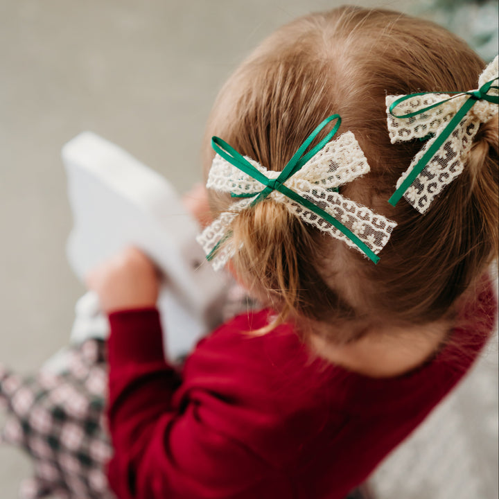 little girl on rocking horse in Christmas plaid dress and crimson cardigan with matching vanilla lace pigtail bows on clips with forest green satin ribbon