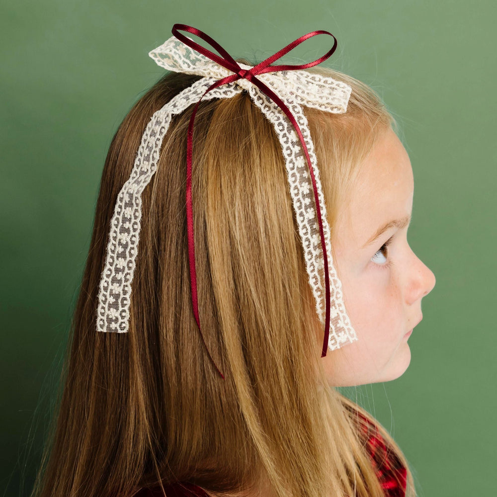 little girl in red velvet Christmas dress paired with long tail cream lace and deep red ribbon bow in clip