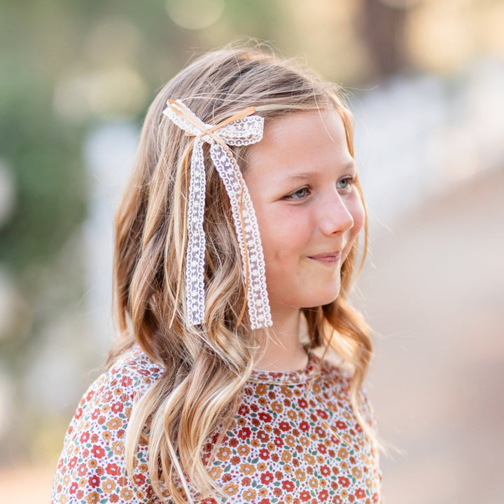 girl in fall ditsy floral velvet long sleeve twirl dress paired with cream, long tail lace bow with mustard ribbon on clip 