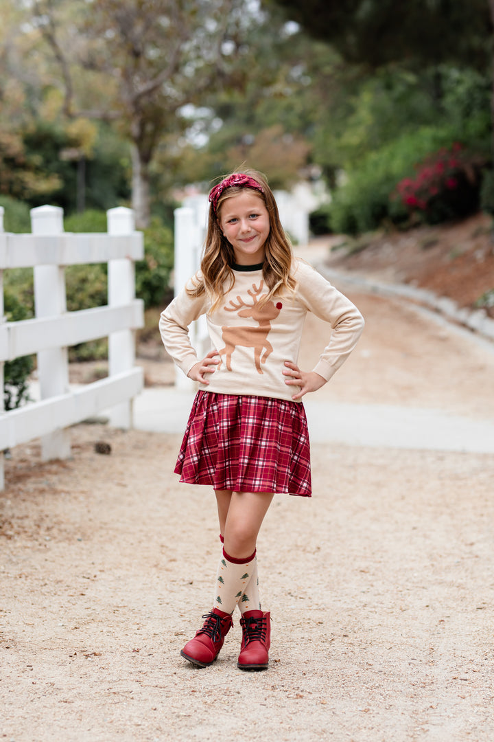 girl on horse trail in cream pullover sweater with reindeer design paired with crimson plaid skirt and headband and coordinating Christmas tree socks