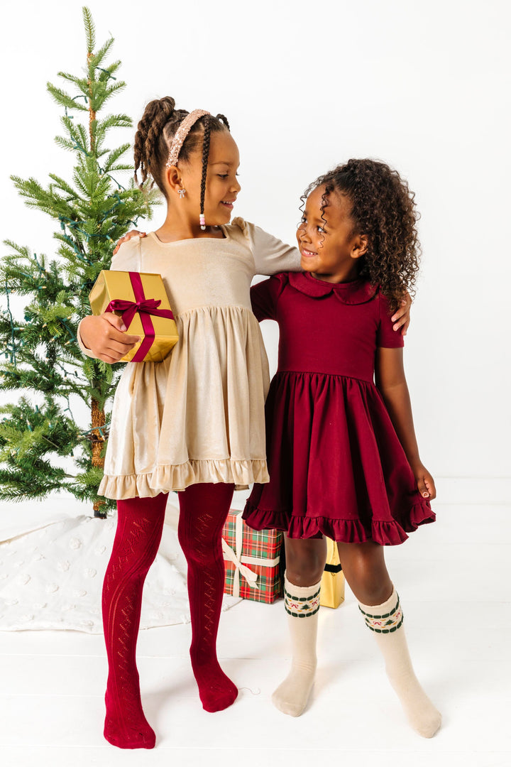 girls in front of Christmas tree in mix and match cream and crimson twirl dresses and accessories