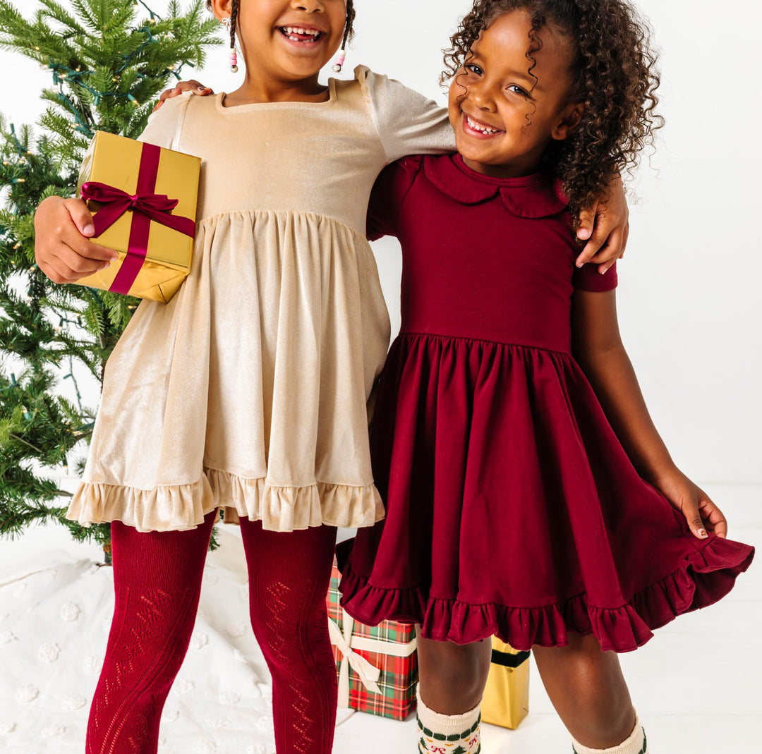 girls in front of Christmas tree in mix and match cream and crimson twirl dresses and accessories