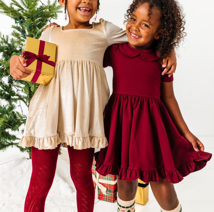 girls in front of Christmas tree in mix and match cream and crimson twirl dresses and accessories