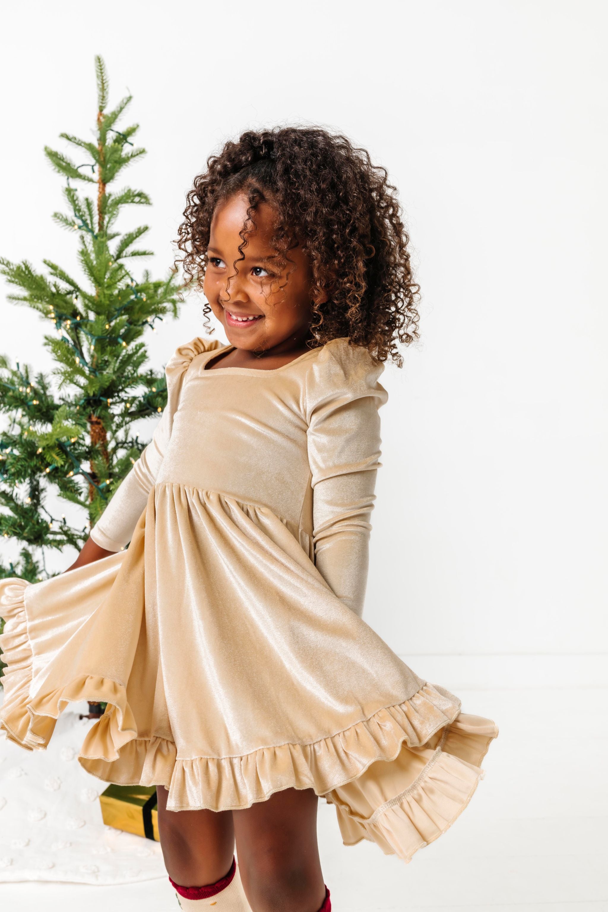 girl twirling in front of Christmas tree in cream velvet long sleeve twirl dress 