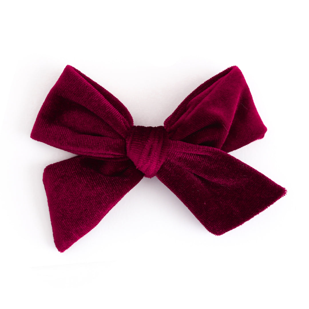 A deep burgundy velvet bow accessory, photographed against a seamless white background.