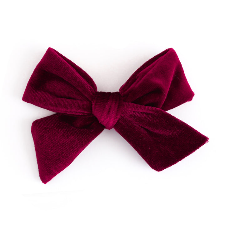 A deep burgundy velvet bow accessory, photographed against a seamless white background.