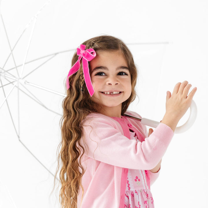 girl wearing hot pink velvet ribbon bow and pink cardigan with spring dress in pink floral wallpaper print