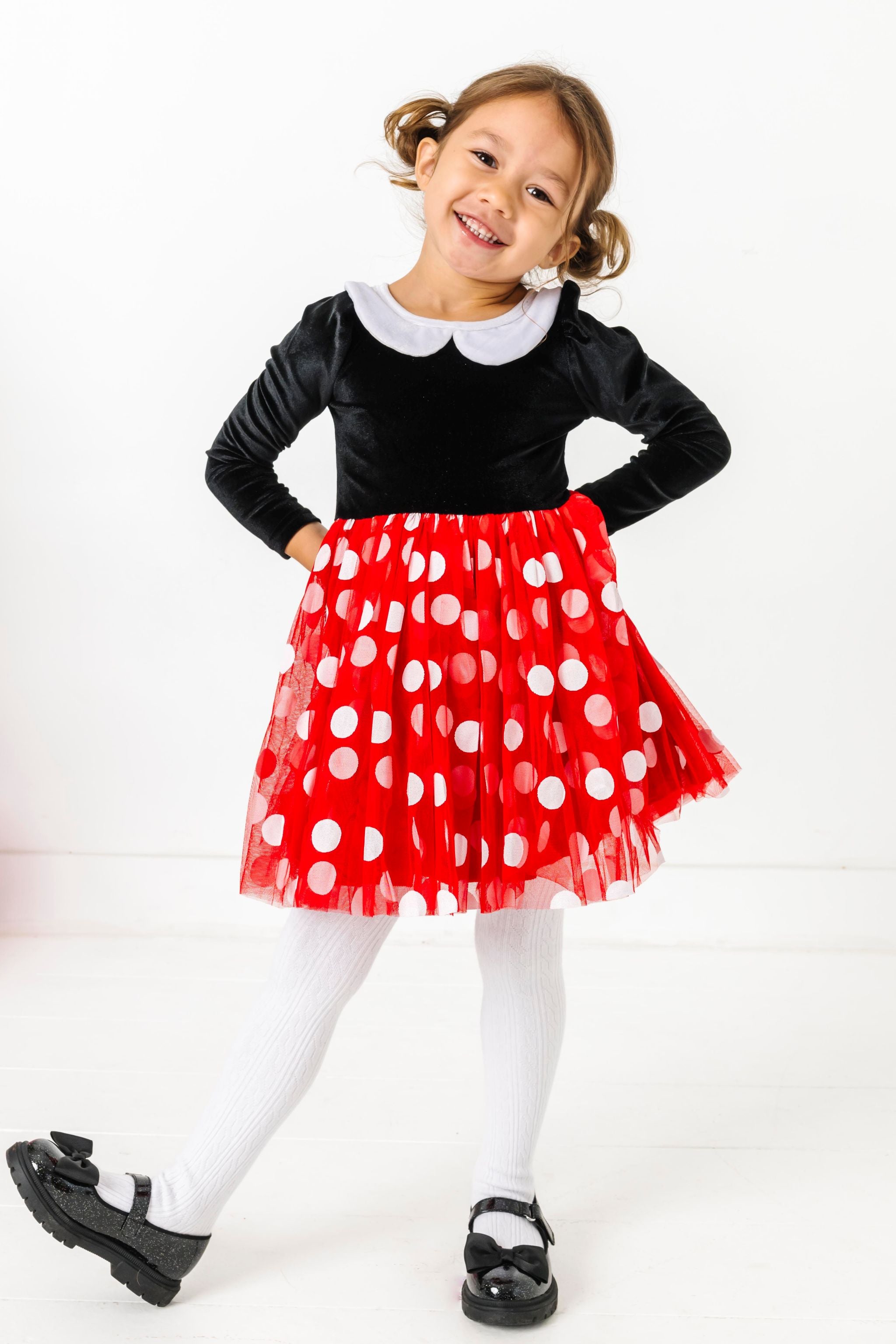 little girl in Minnie inspired twirl dress with black velvet long sleeve bodice, white velvet collar and red tulle skirt with white polka dots paired with white cable knit tights