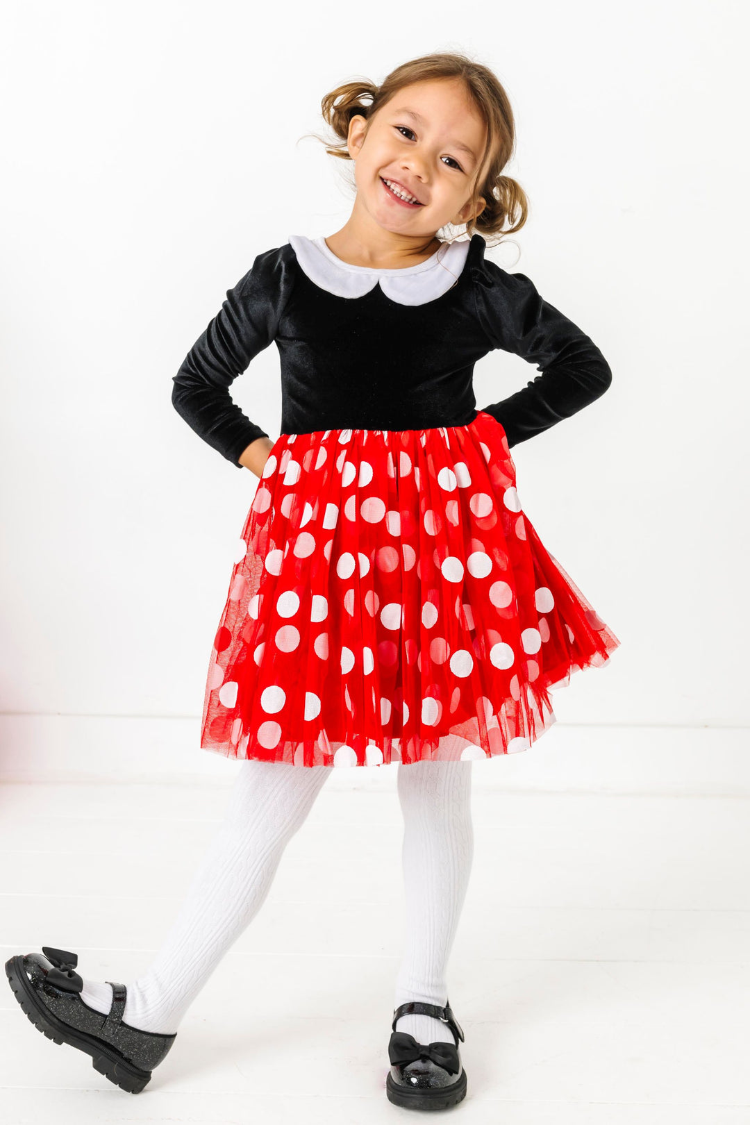 little girl in Minnie inspired twirl dress with black velvet long sleeve bodice, white velvet collar and red tulle skirt with white polka dots paired with white cable knit tights