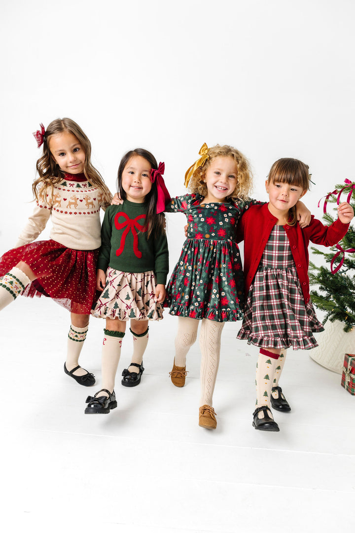 four young girls wearing mix and match dresses, skirts, socks, bows and sweaters in shades of cream, crimson and forest green with vintage Christmas vibes