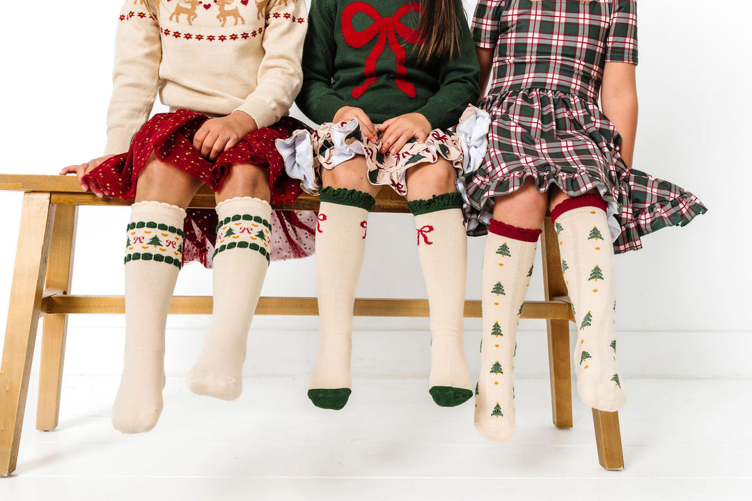 three girls with cream knee high socks featuring Christmas trees and bows to match Christmas outfits