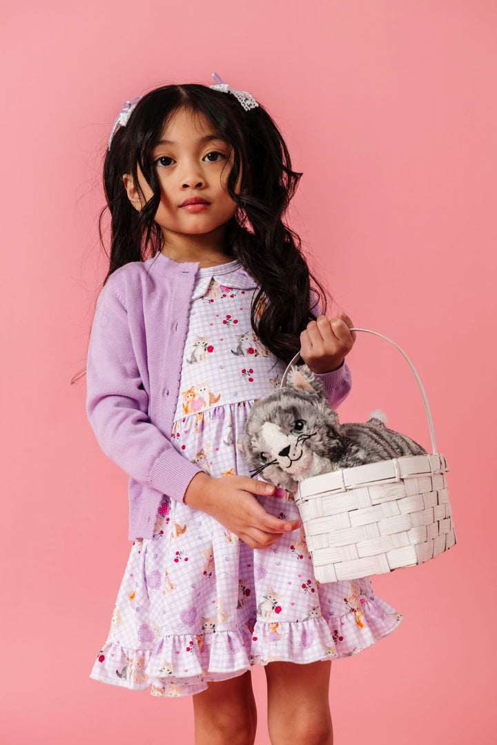 little girl holding basket with stuffed kitten wearing lavender gingham twirl dress with vintage kitten print and matching lavender cardigan