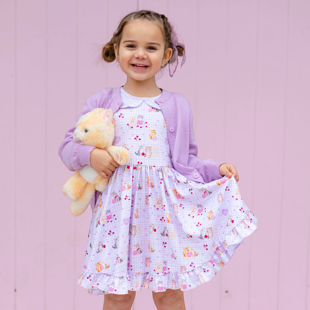 little girl holding stuffed kitten in lavender gingham collared twirl dress with vintage kitten print paired with lavender cotton knit cardigan and matching sheer bow
