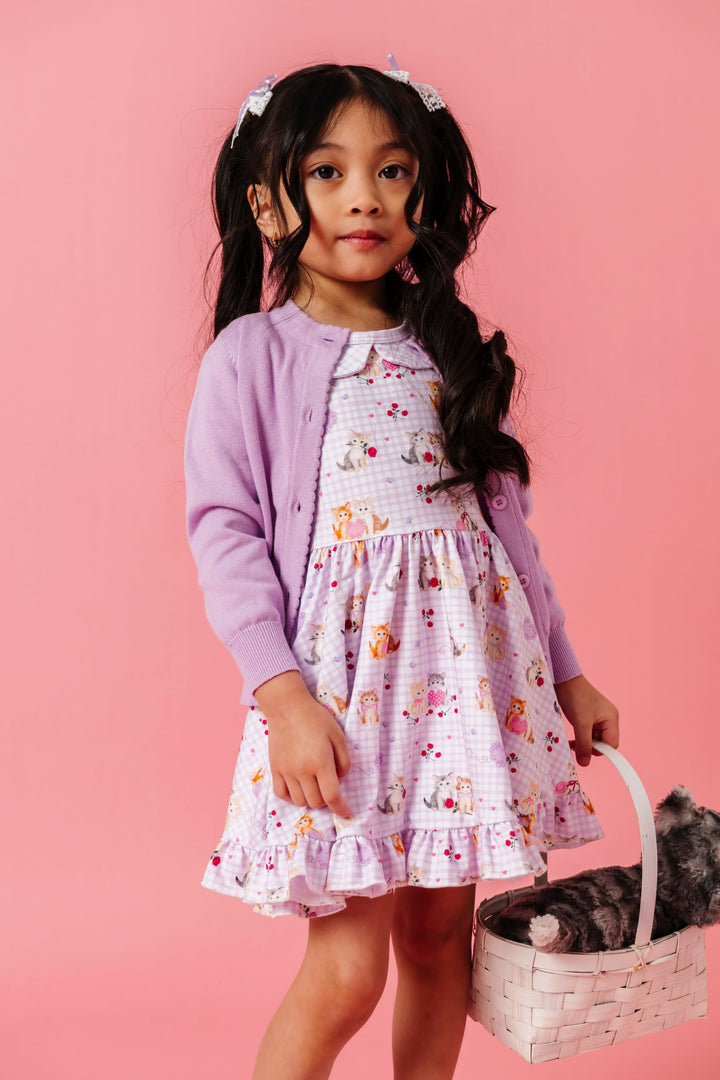 little girl holding basket with stuffed kitten wearing lavender gingham twirl dress with vintage kitten print and matching lavender cardigan