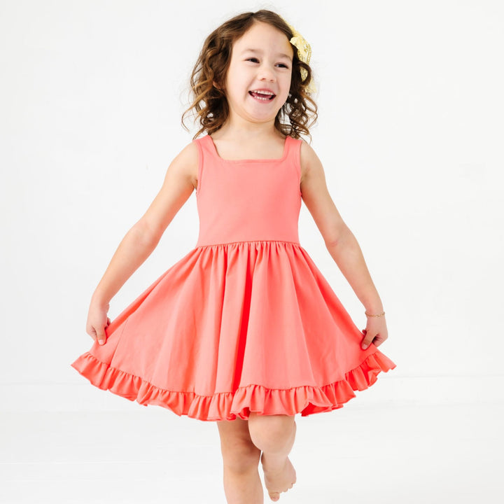 little girl in square neck sleeveless twirl dress with ruffle hem in shade of coral pink 