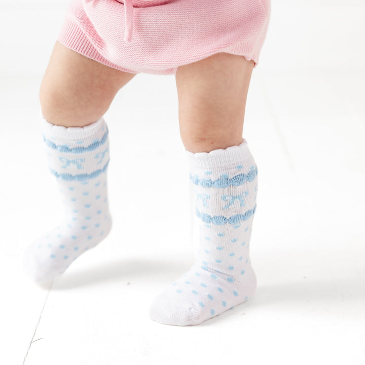 baby walking in white knee high socks with a scallop trim and blue polkadots and bows on them