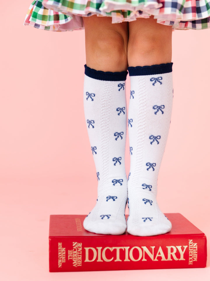 girl wearing white knee high socks with navy bows and navy scalloped trim standing on dictionary