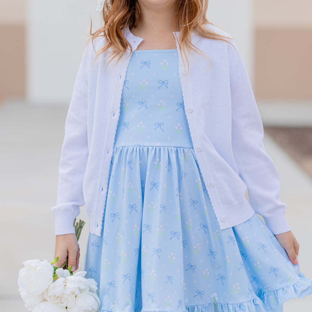 girl in white cotton knit scallop trim cardigan and blue twirl dress with bows and flowers printed on it