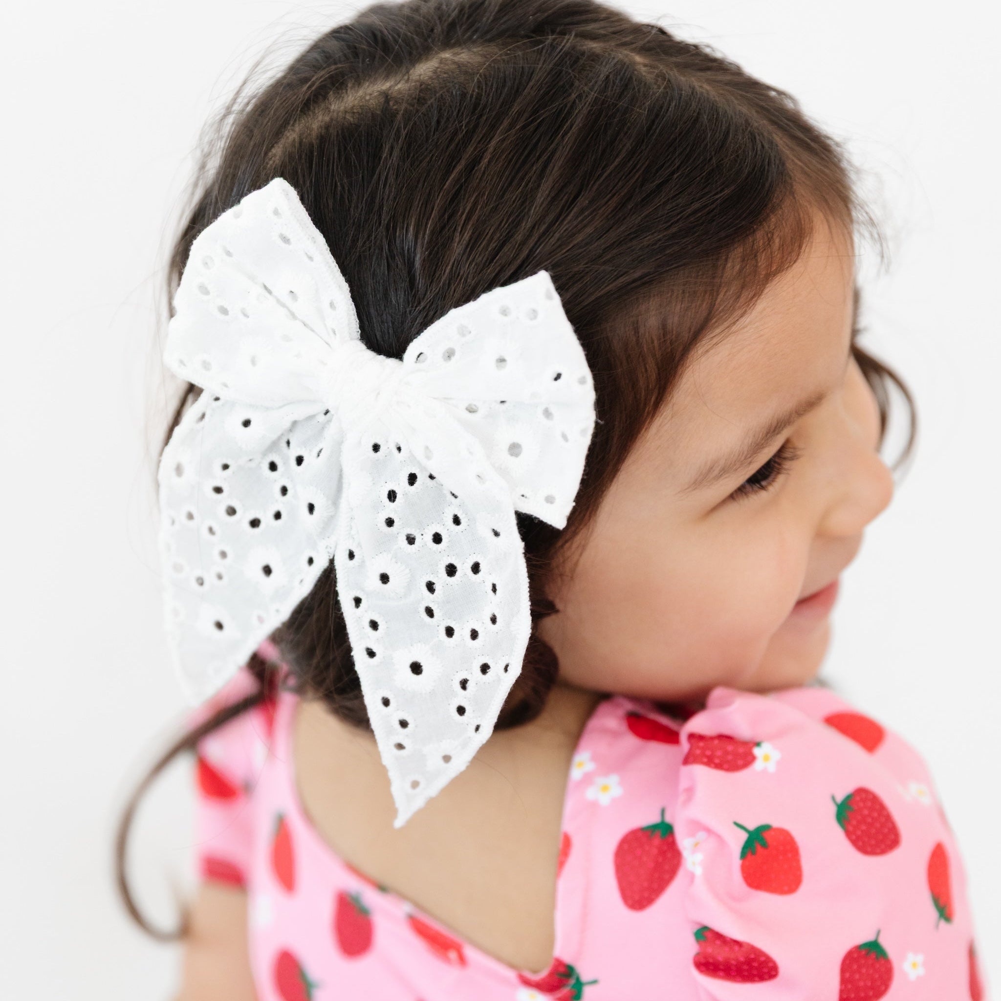 photo of white eyelet large bow on clip on girl wearing pink dress with strawberry print