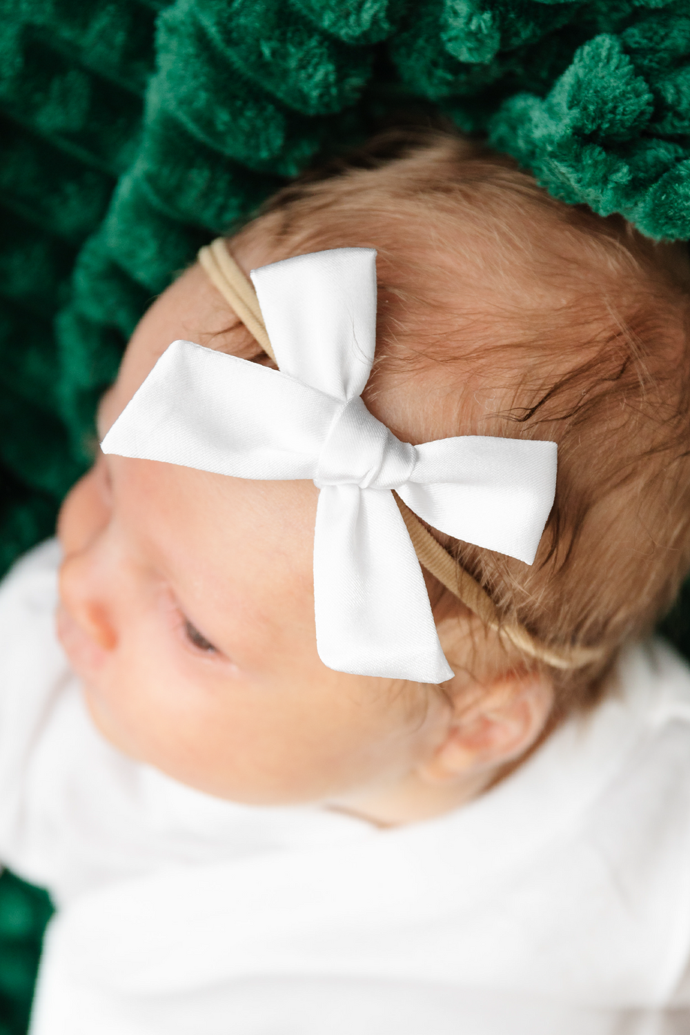 Baby with a white bow in hair against a green textured background
