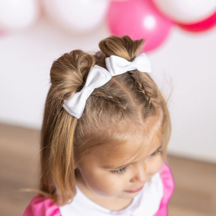 little girl in pink twirl dress and white satin pigtail bows