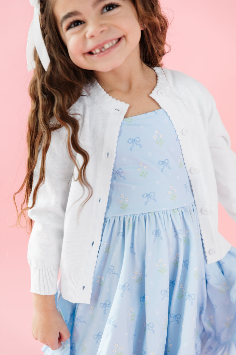 girl wearing white cotton knit, button front cardigan and matching blue bow printed twirl dress