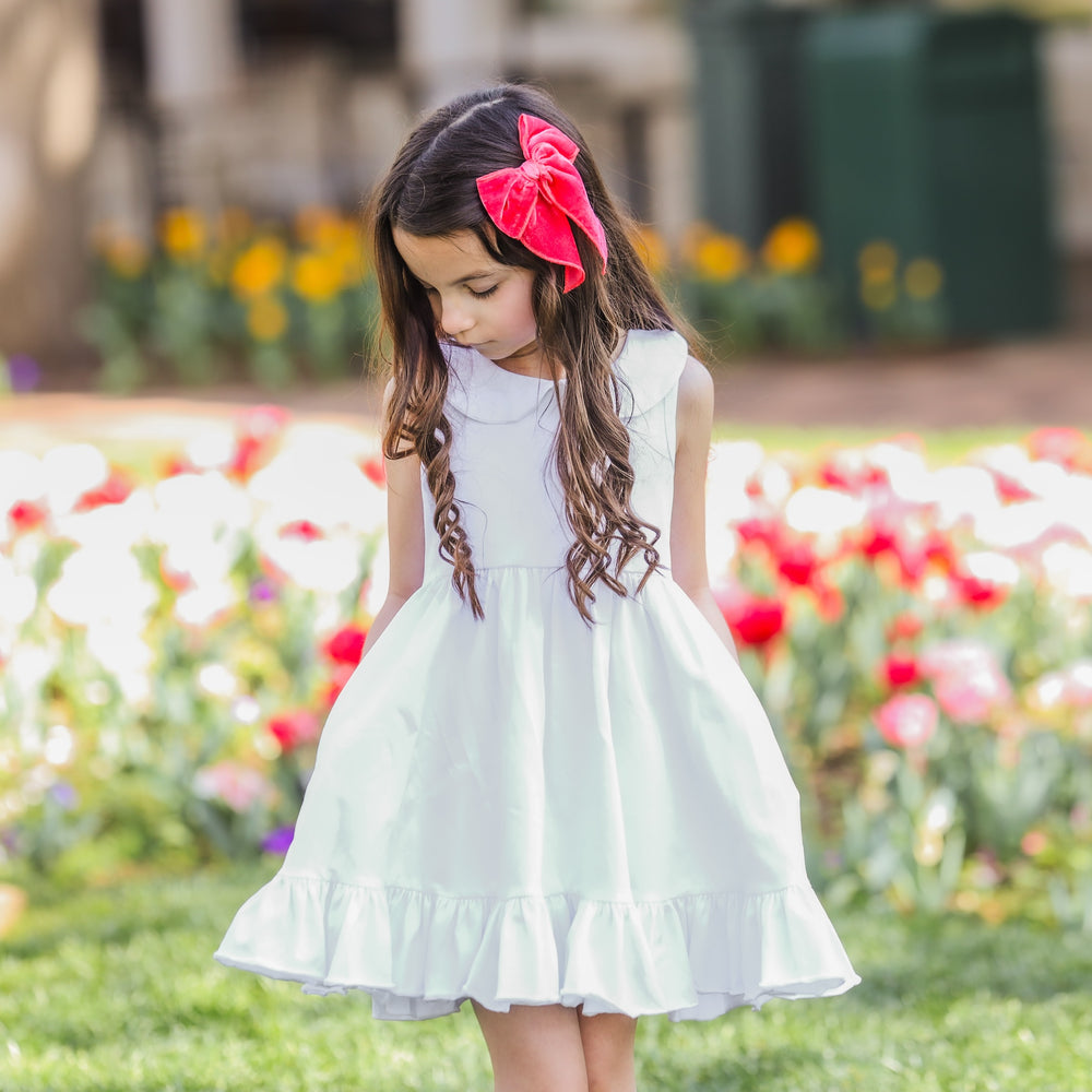 little girl outside with hands in pocket of white summer dress